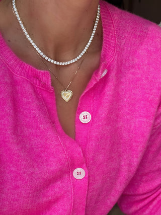 Woman wearing a tennis necklace and gold heart charm pendant necklace jewelry stack 